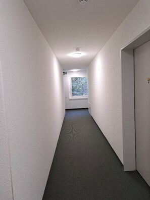 A narrow hallway with a carpeted floor, white walls, and a door on the right.