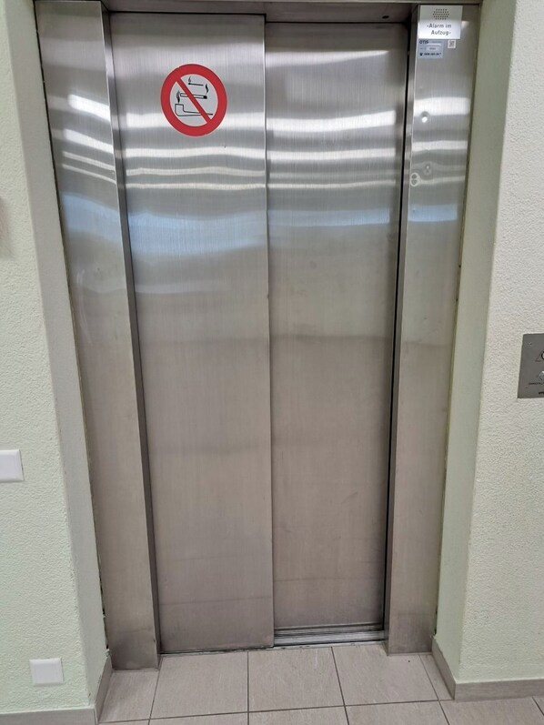 Ein Aufzug mit einem Rauchverbotsschild, einer Bedienfeld-Leiste und einem an der Wand befestigten Lichtschalter.