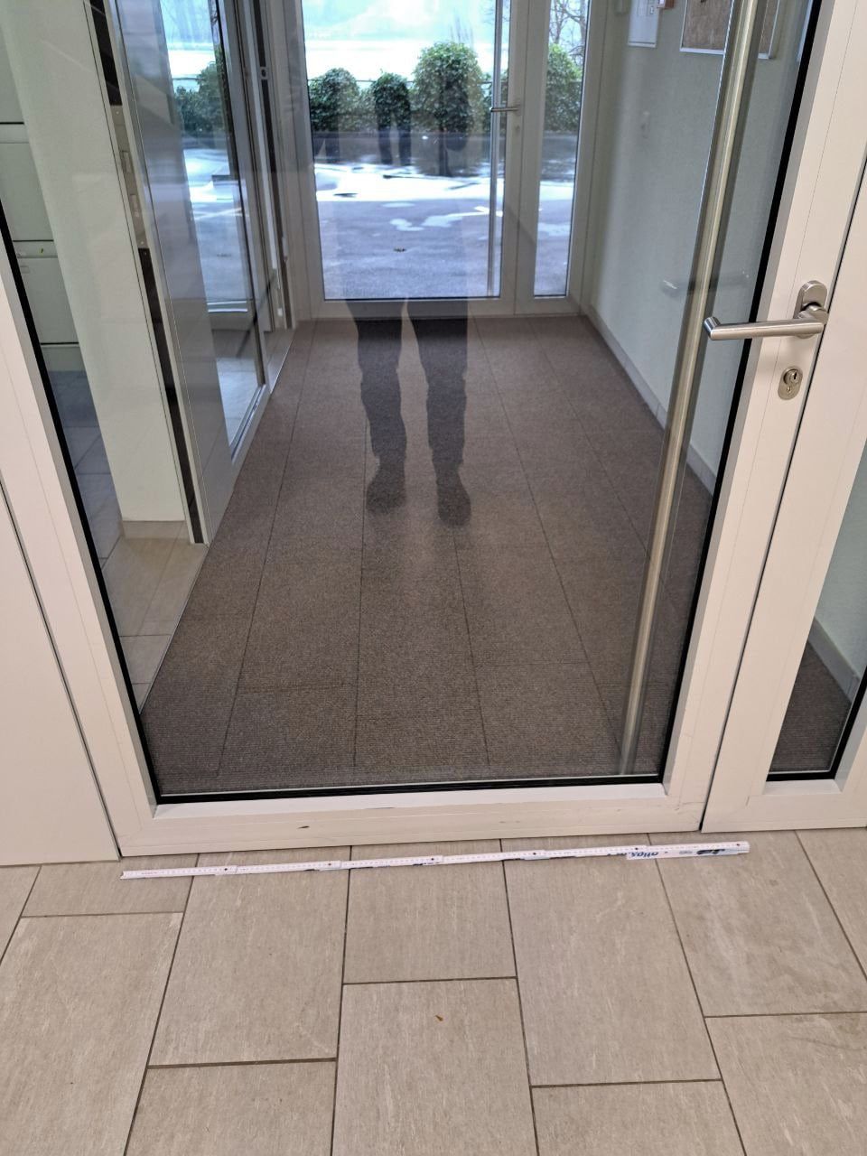 A glass door with a metal handle, leading to a tiled floor area.