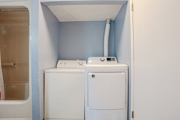 A laundry room with two white washing machines and a dryer, a white door, and a blue wall. - Enjoy Peace, No Crowds at the beachfront Saltwater Sanctuary, Walk to Tootsie's (Panama City Beach)