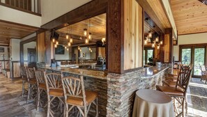 Een ruime bar met een stenen toonbank, houten stoelen en hangende lampen.