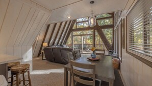 Een gezellige zolderkamer met een eettafel, stoelen en een bank. Grote ramen bieden uitzicht op de omgeving.