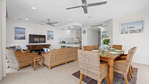 Una sala de estar moderna con muebles de mimbre, una mesa de comedor preparada para seis personas y una cocina al fondo.