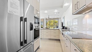 Una cocina moderna con electrodomésticos de acero inoxidable, un ventanal y vistas al verdor exterior.