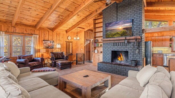 A cozy log cabin interior with a fireplace, wooden furniture, and a television mounted above it. - The Woodhaven Cabin In Massanutten (McGaheysville)
