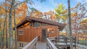 A wooden cabin with a wooden deck, surrounded by trees with autumn foliage. - The Woodhaven Cabin In Massanutten (McGaheysville)