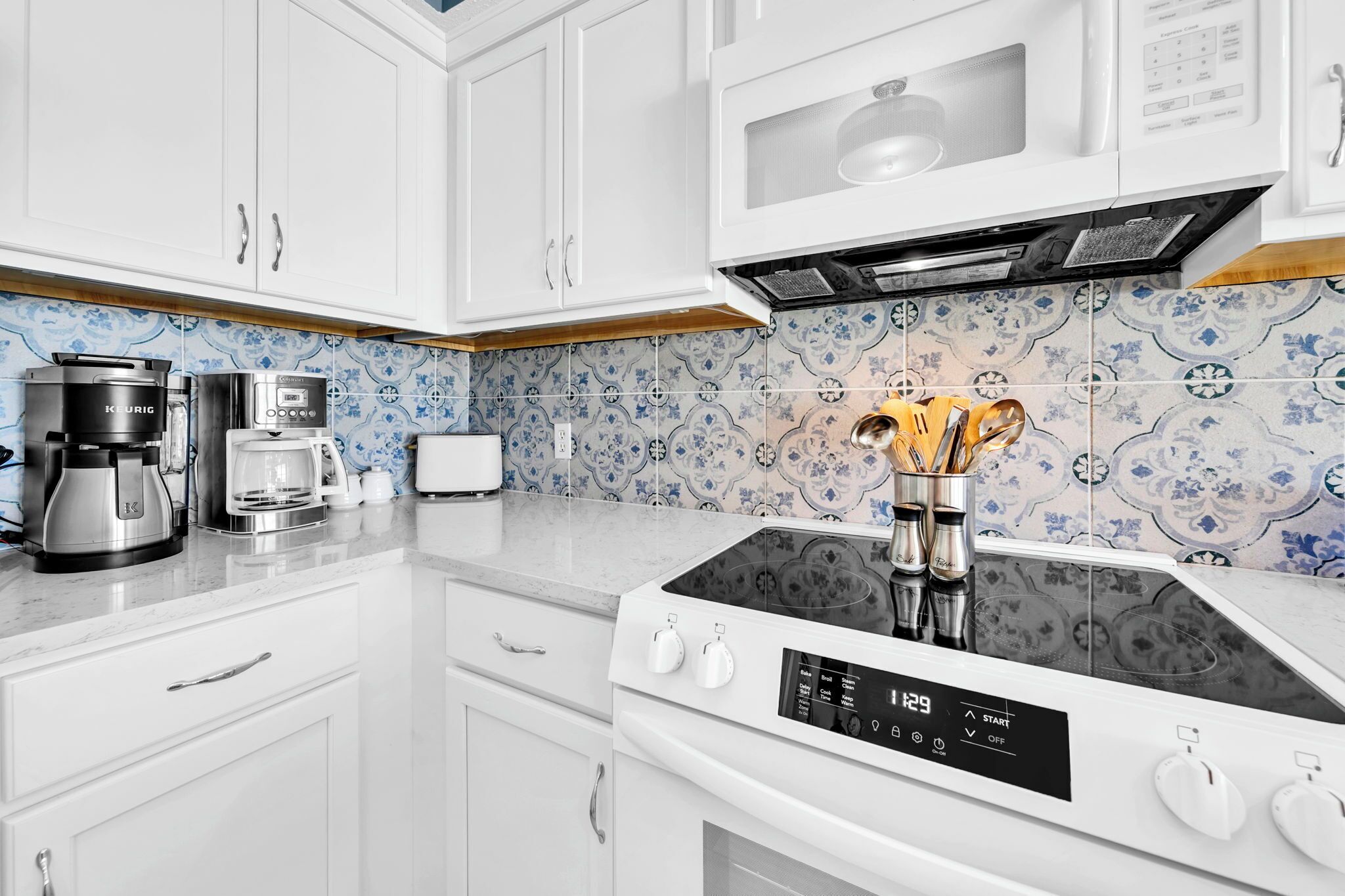 A modern kitchen with white cabinets, a built-in microwave, a coffee maker, and a stove with a digital control panel.