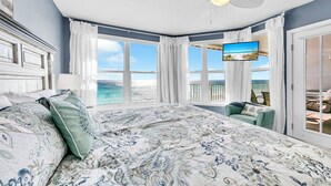 Une chambre avec un grand lit, un ventilateur de plafond, une télévision et une vue sur l’océan.