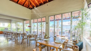 A spacious indoor dining area with wooden tables and chairs, large windows, and potted plants. - 2BR Family Haven in Secure Resort Community with Beach Club Access (Isla Mujeres)