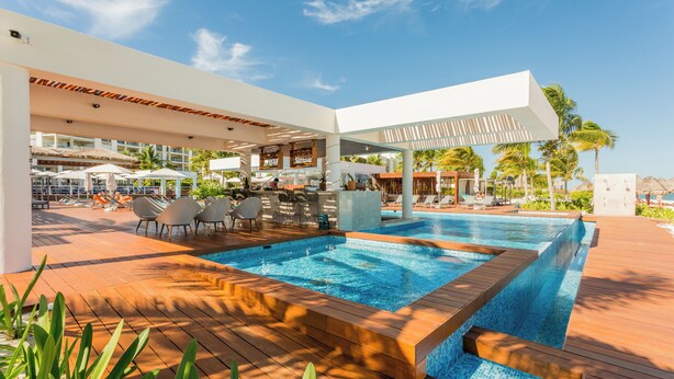 A modern pool area with lounge chairs and umbrellas, surrounded by palm trees and a clear sky. - 2BR Family Haven in Secure Resort Community with Beach Club Access (Isla Mujeres)