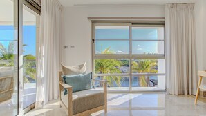 A modern room with a large sliding glass door leading to a balcony with a view of palm trees and the sea. - 2BR Family Haven in Secure Resort Community with Beach Club Access (Isla Mujeres)