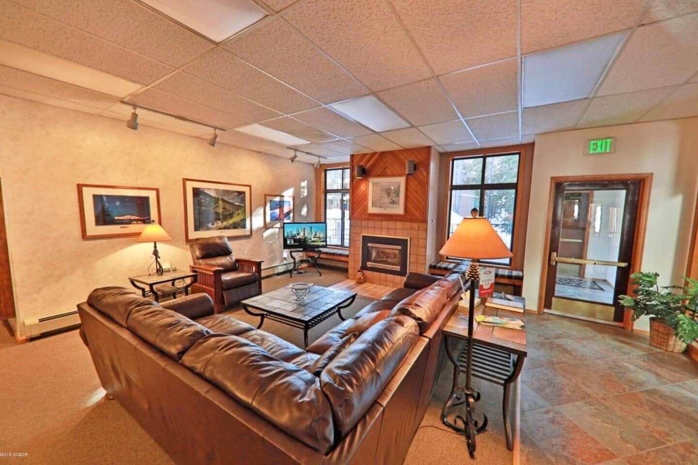 A lobby with a leather sofa, a coffee table, a fireplace, and framed pictures on the walls.
