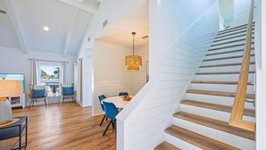 A modern interior with a wooden staircase, a dining area with blue chairs, and a view of the outdoors. - Pearl Sands - Private Pool and Golf Cart! (Destin)