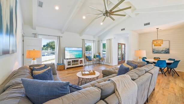 A spacious living room with a large sofa, a television, and a dining area with blue chairs. - Pearl Sands - Private Pool and Golf Cart! (Destin)