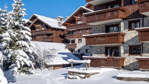 Eine mehrstöckige Holzchalet mit Balkonen, umgeben von schneebedeckten Bäumen und einem klaren, blauen Himmel.