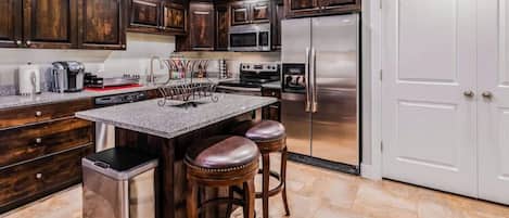 Una cocina con armarios de madera oscura, electrodomésticos de acero inoxidable, encimera de granito y una zona con taburetes de bar.