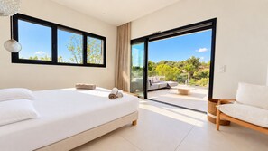 Un dormitorio moderno con una cama grande, un sofá y vistas a un jardín a través de un ventanal corredero.