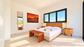 A modern bedroom with a large bed, a wooden bench, a bedside table, a mirror, and a window with a view. - Villa Alimea Di San Ciprianu (sainte lucie de porto vecchio)