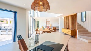 A modern kitchen with a central island, a dining area with a wooden table, and a staircase leading to an upper level. - Villa Alimea Di San Ciprianu (sainte lucie de porto vecchio)