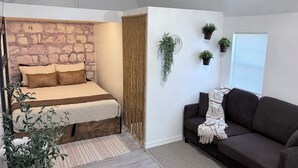 A bedroom with a stone wall, a bed with brown pillows, a dark sofa, and several potted plants. - Bohemian and Romantic Cabin (Ocala)