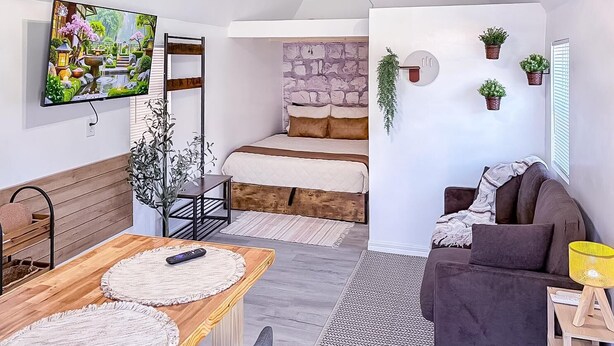 A cozy living room with a wooden coffee table, a sofa, a TV mounted on the wall, and a stone wall in the background. - Bohemian and Romantic Cabin (Ocala)