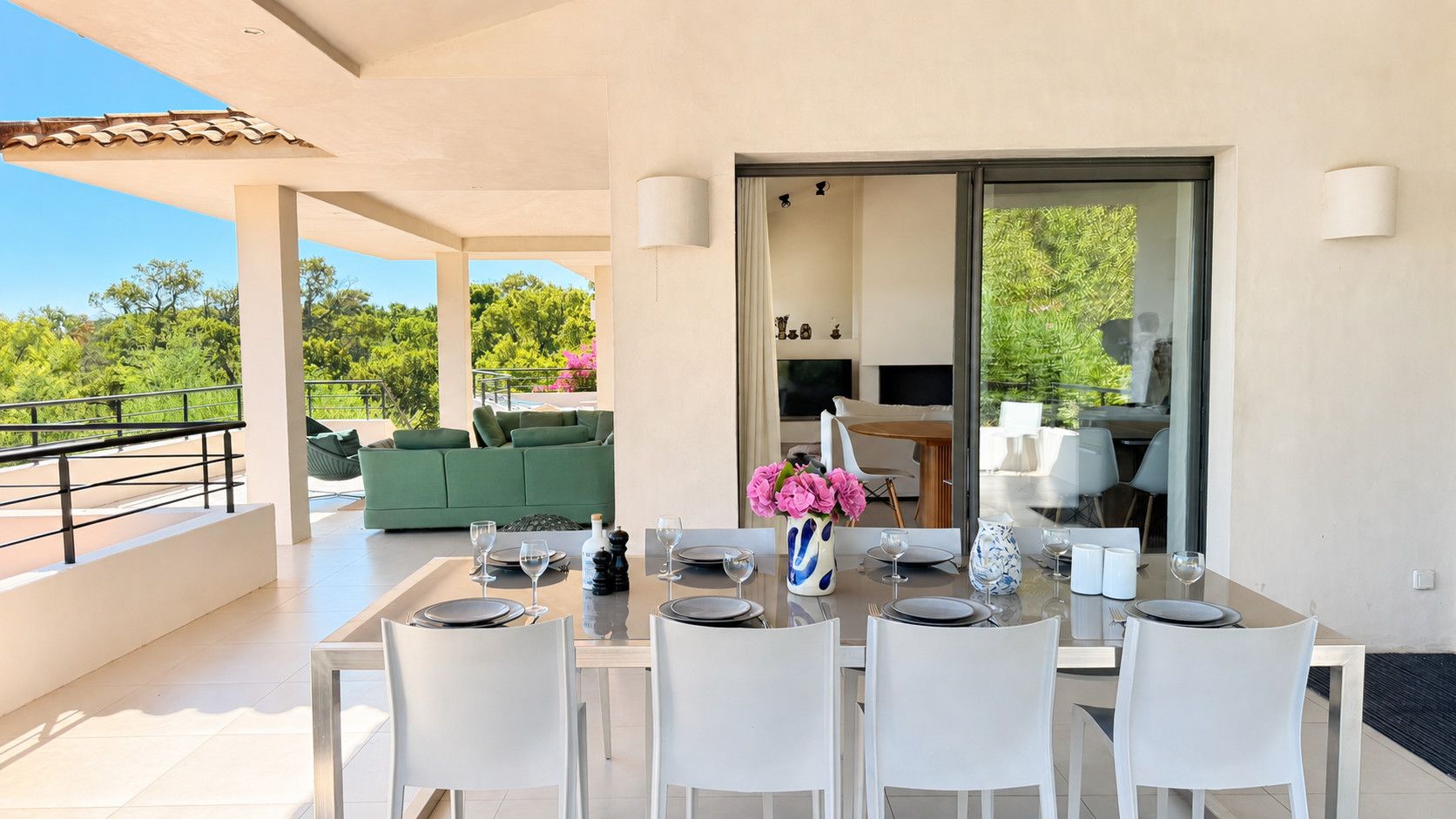 Un espace de restauration en plein air avec une table dressée pour six personnes, entourée de chaises blanches, et un canapé vert en arrière-plan.