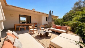 Een terras buiten met een bank, stoelen, een tafel en een houten bankje.