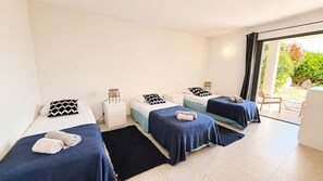 Habitació d'hotel amb tres llits, un escriptori petit, una cadira i vista a l'exterior.