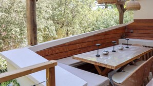 Een terras buiten met houten banken, een tafel met stoelen en hangende lichten.