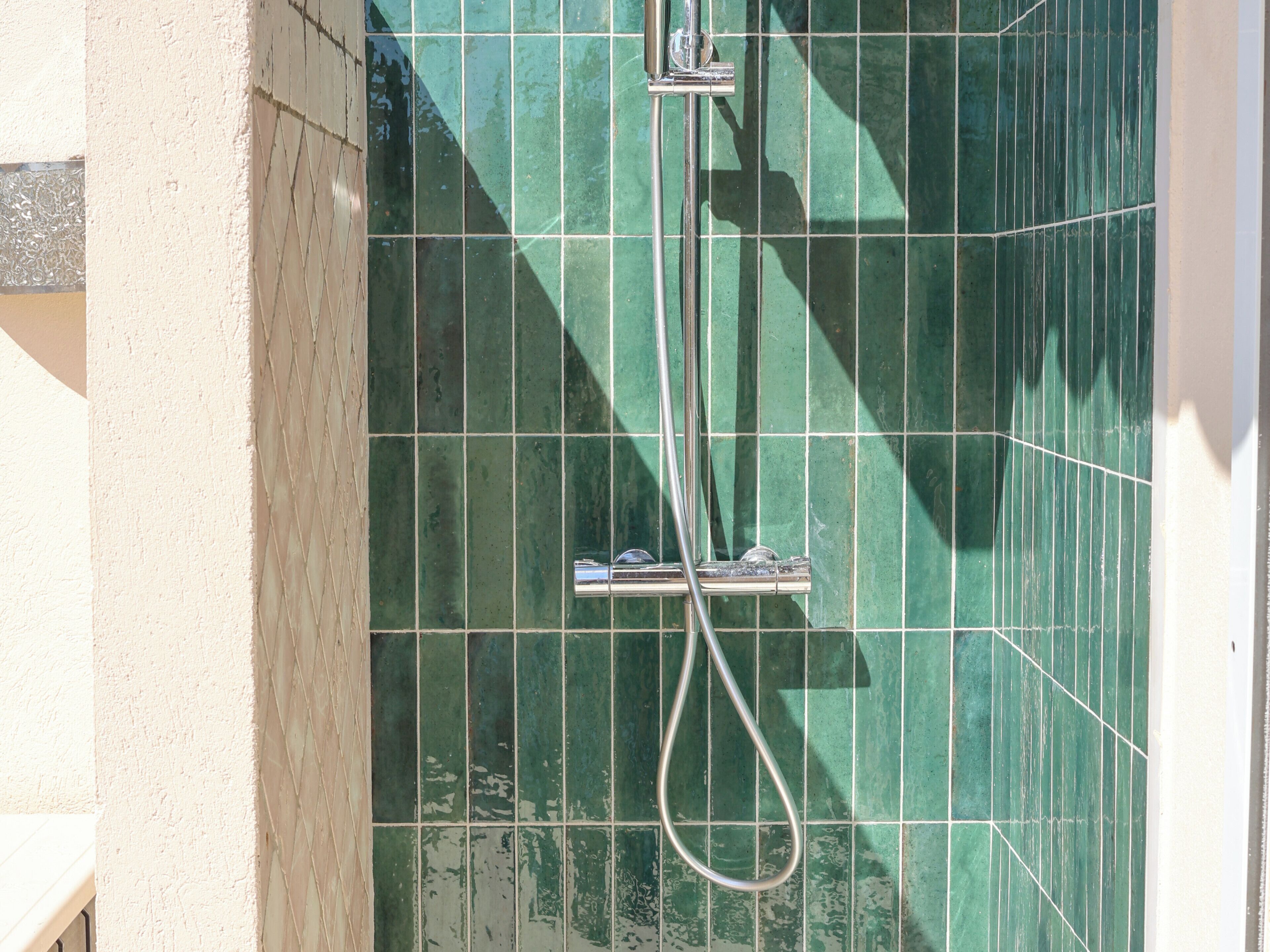 A shower area with green tiles and a chrome showerhead.