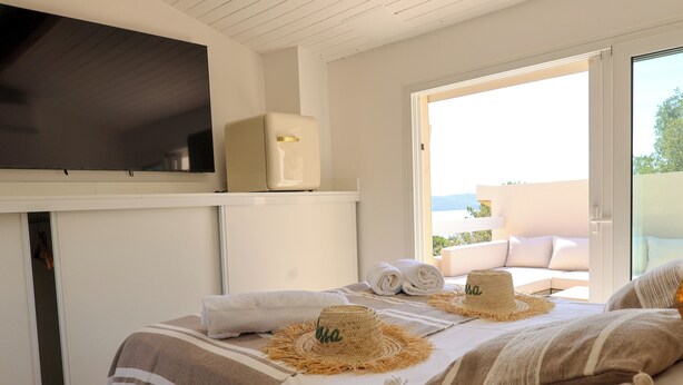 Een hotelkamer met een bed, een televisie, een balkon met uitzicht, en een deur naar buiten.