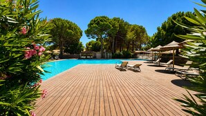 Eine Holzterrasse mit Schwimmbecken, umgeben von Bäumen und beschattet durch Sonnenschirme.