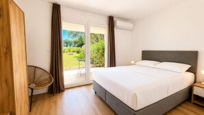 Ein Schlafzimmer mit einem Bett, einem Sessel, einem Tisch und einer Glastür zum Außenbereich.