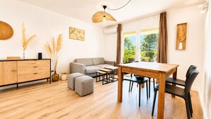Ein modernes Wohnzimmer mit einer Couch, Hocker, einem Esstisch mit Stühlen, einer Holzkommode und Dekorationselementen.