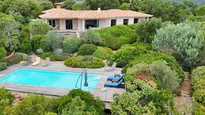 A house with a swimming pool surrounded by lush greenery and a wooden deck. - Villa A Pinedda Mare (Zonza)