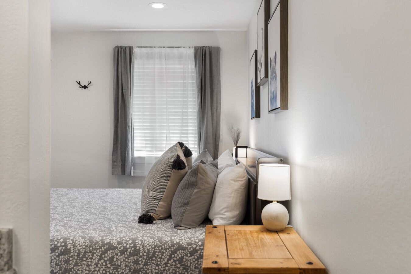Une chambre à coucher avec un lit, des oreillers, une table de chevet, une lampe et une fenêtre avec des rideaux.