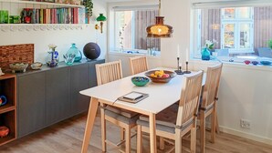 Een eethoek met een witte tafel, vier houten stoelen, een schaal fruit en een notitieboek.