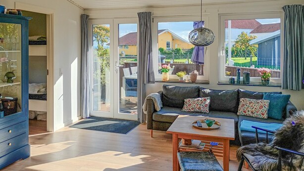 Een gezellige woonkamer met een bank, een tafel en een stoel. Er is een blauwe kast en een glazen deur die leidt naar een balkon.
