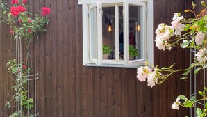 Een houten gebouw met een raam en een metalen plantenhouder met roze bloemen.