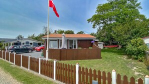 Een omheinde achtertuin met een houten terras, een rode vlag en een huis met een pannendak.