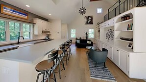 Une cuisine spacieuse dotée d’un îlot central, de tabourets de bar et d’un coin repas. Un escalier mène à un niveau supérieur où se trouve un balcon.