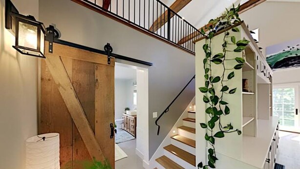 Un escalier avec des marches en bois et une rampe noire, menant à un deuxième étage doté d’une balustrade blanche.