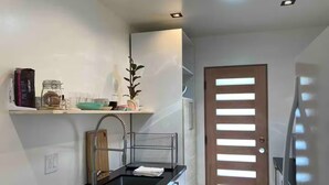 A modern kitchen with a black countertop, a sink, a wooden cutting board, and a shelf with various items. - Charming 3-bedroom house in welcoming Torrance with AC (Torrance)