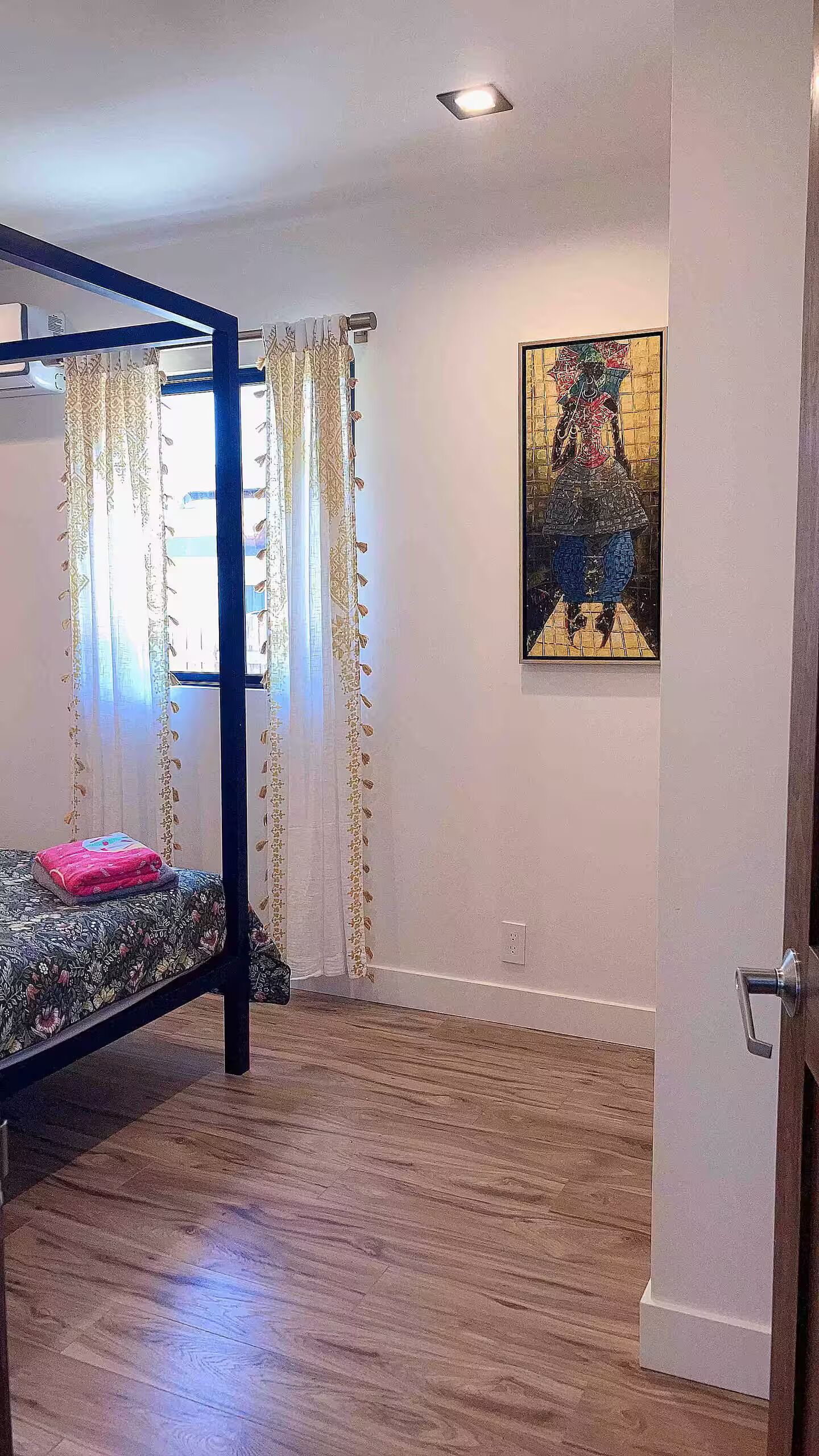 Un dormitorio con una cama nido, cortinas estampadas, un cuadro en la pared y suelo de madera.
