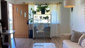A living room with a wooden floor, a sofa, a coffee table, a dining table with chairs, and a window with plants. - Charming 3-bedroom house in welcoming Torrance with AC (Torrance)