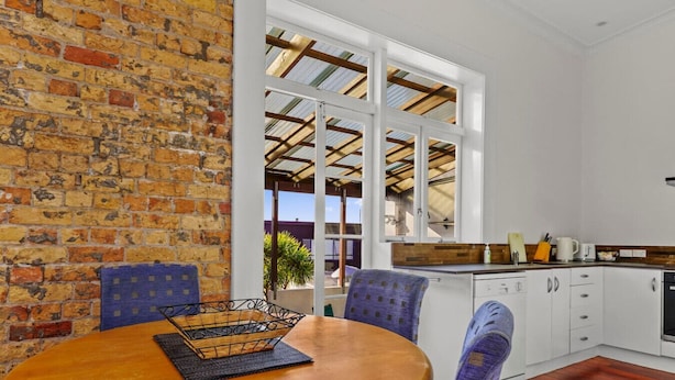 A dining area with a brick wall, a wooden table, and two chairs. - Gorgeous New York-Style Loft with Deck and Air-con (Auckland Central Suburbs)