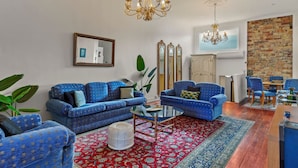 A living room with blue patterned sofas, a round coffee table, a red patterned rug, and a brick wall. - Gorgeous New York-Style Loft with Deck and Air-con (Auckland Central Suburbs)