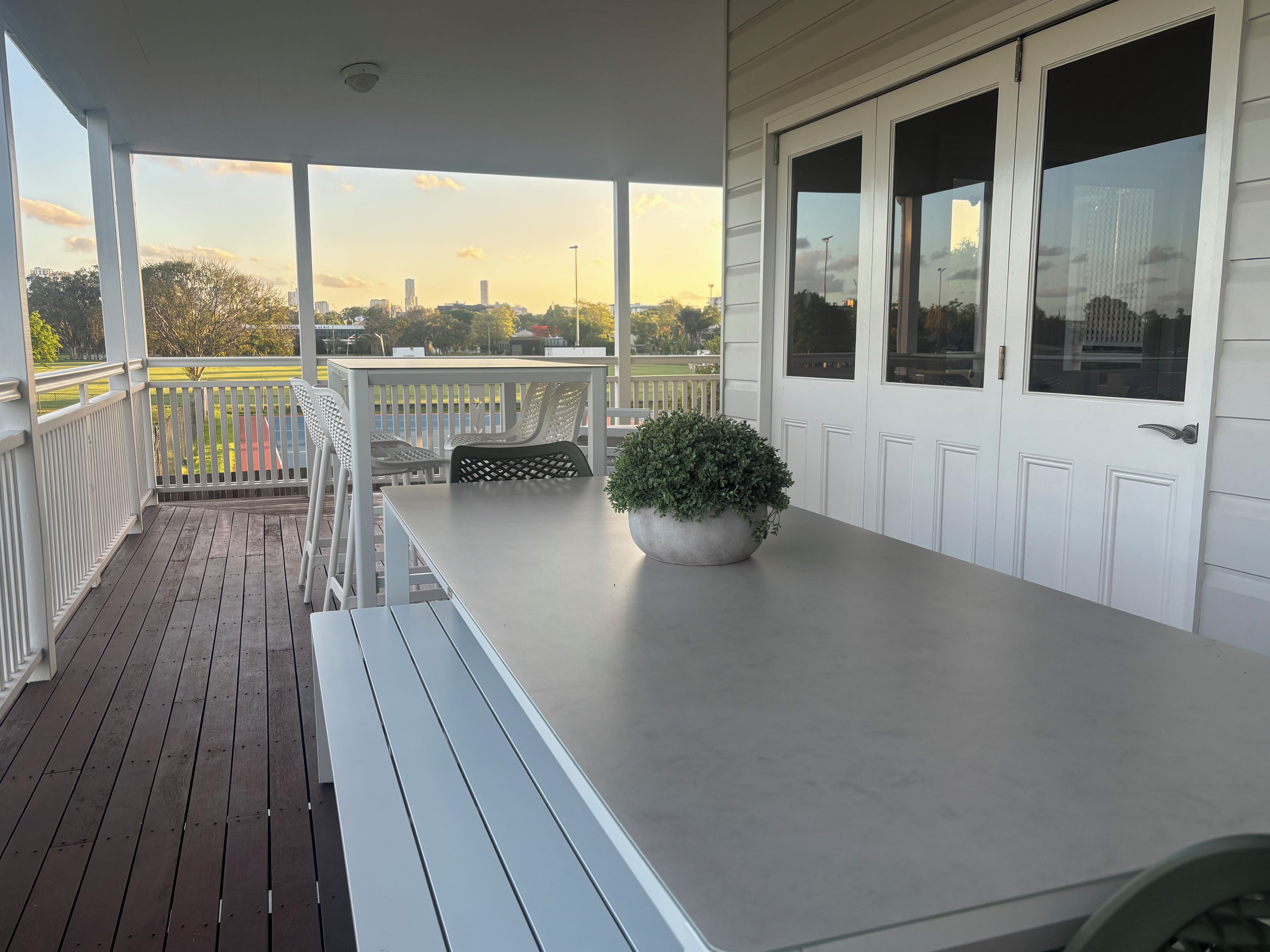 A covered outdoor area with a table and chairs, a potted plant, and a view of the cityscape.