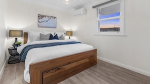 Een slaapkamer met een houten bed, twee nachtkastjes met lampen, een wandairconditioner en een raam met uitzicht.