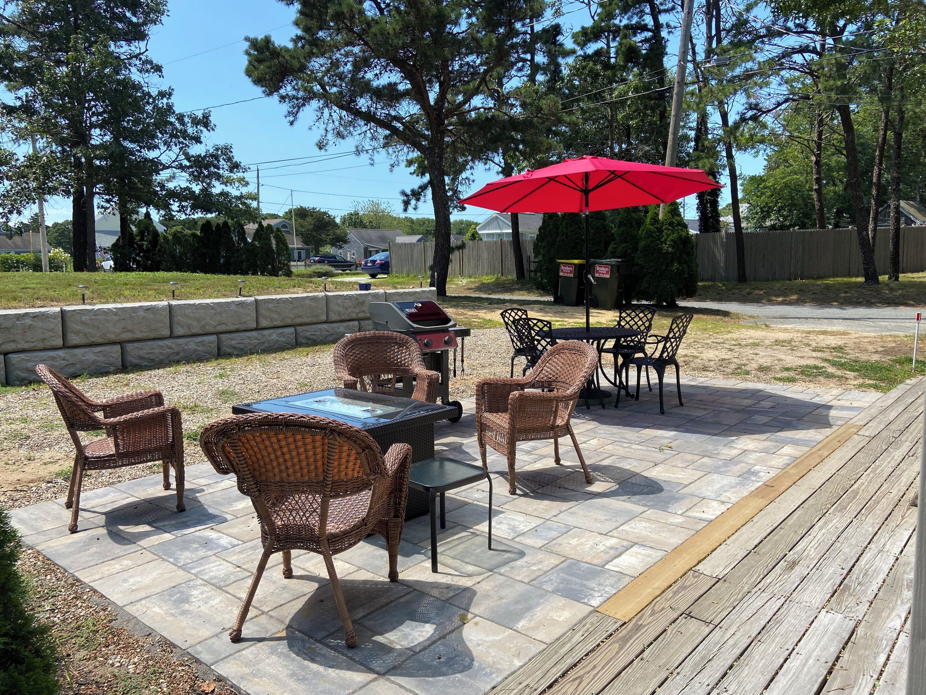 An outdoor patio with wicker furniture, a grill, and a red umbrella.